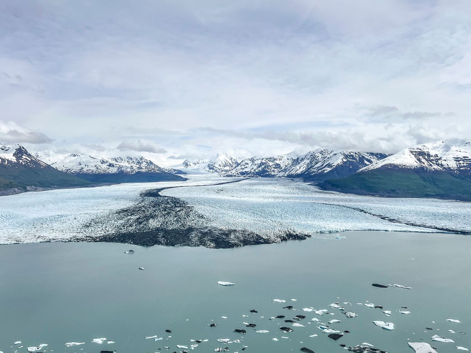 Panoramic view of a glacial bay with floating ice and snow-covered mountains in the background.