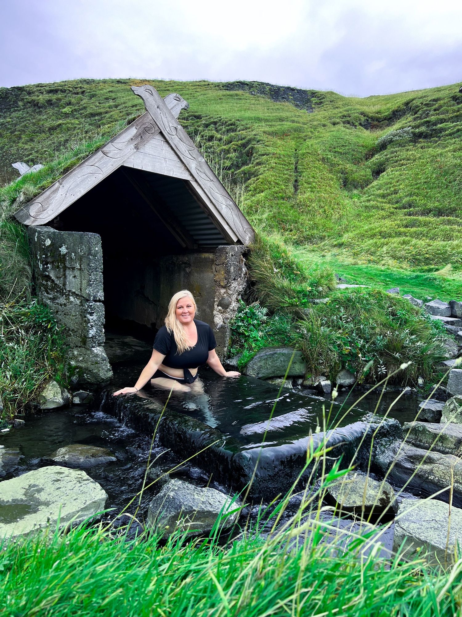 Stone shelter nestled in green rolling hills alongside a rocky stream in rural countryside.