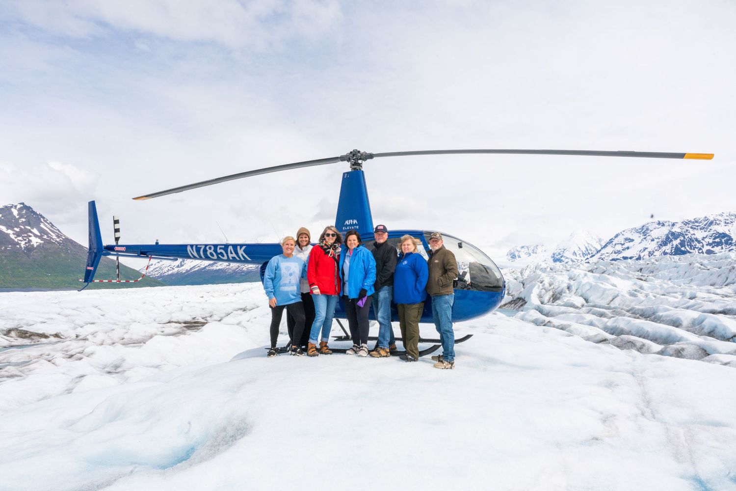 A helicopter tour group poses in front of snowy mountain landscapes in Alaska at Knick Glacier.