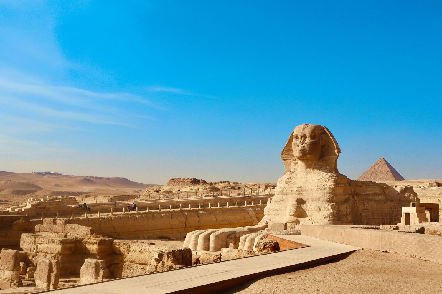 Great Sphinx of Giza with pyramids in background against bright blue sky in Egypt.