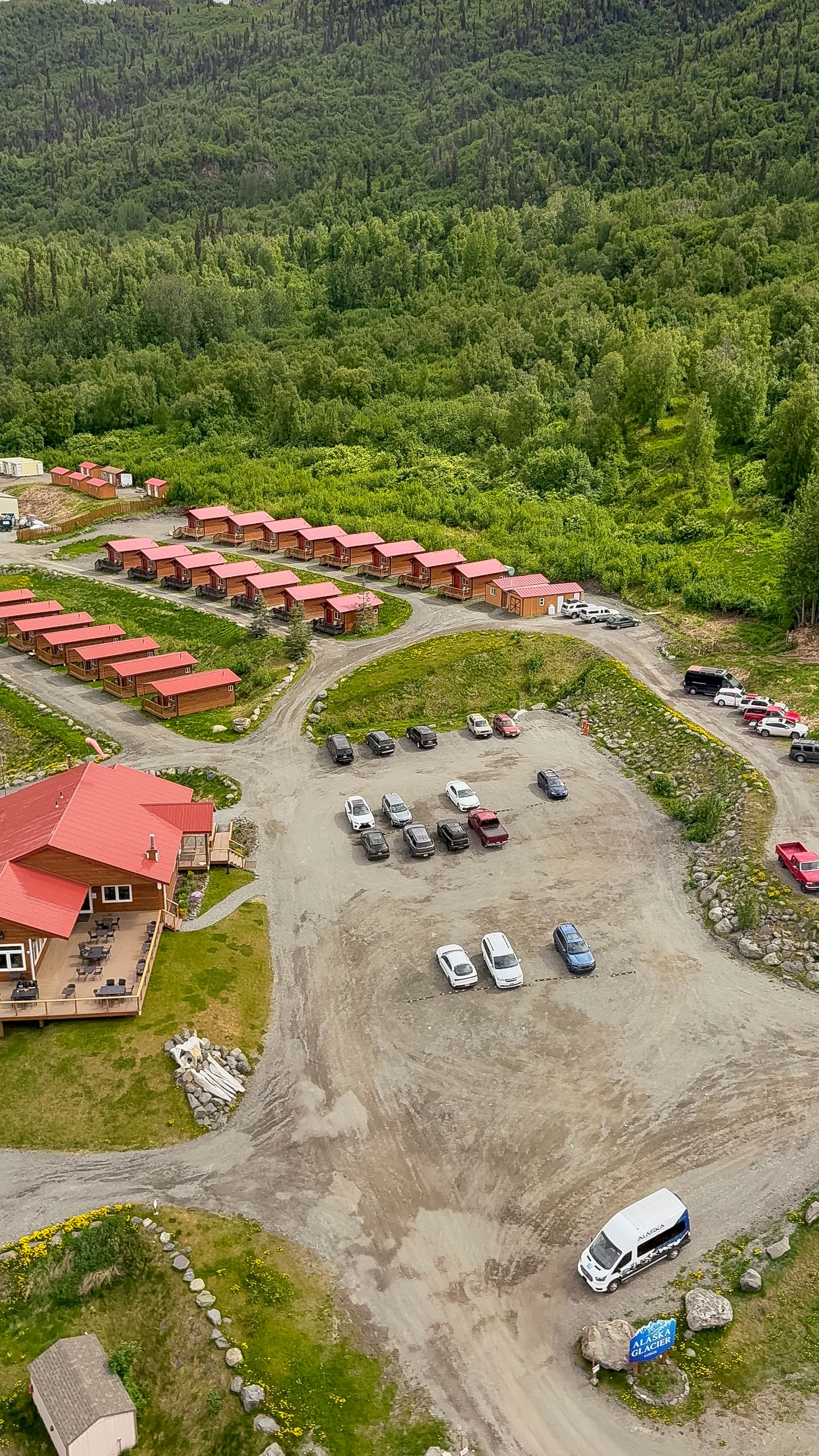Aerial view of red-roofed cabins arranged in rows with parking area in mountainous wilderness setting.