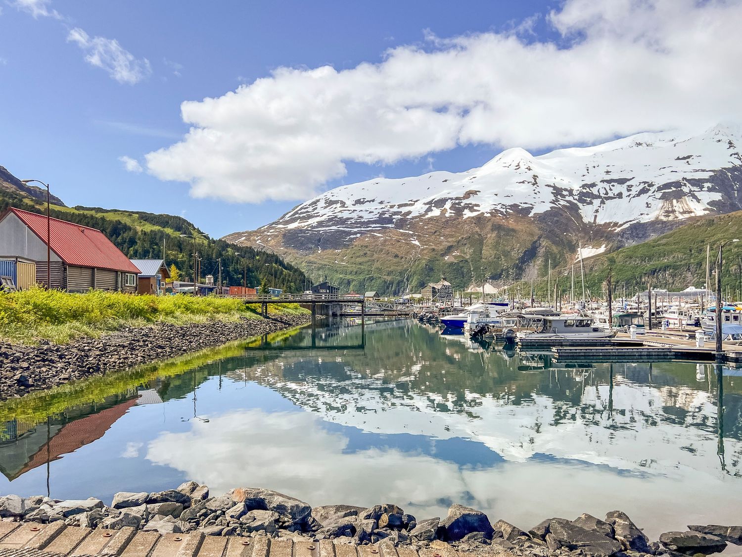 Scenic harbor view with boats docked against a backdrop of snow-capped mountains and blue skies, Whittier Alaska.