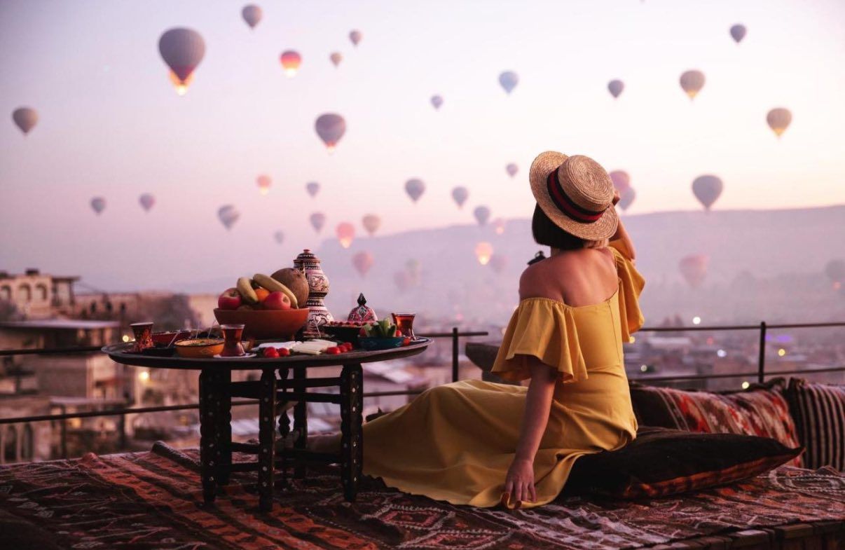 Hot air balloons floating over desert landscape at dawn with viewing platform in foreground.