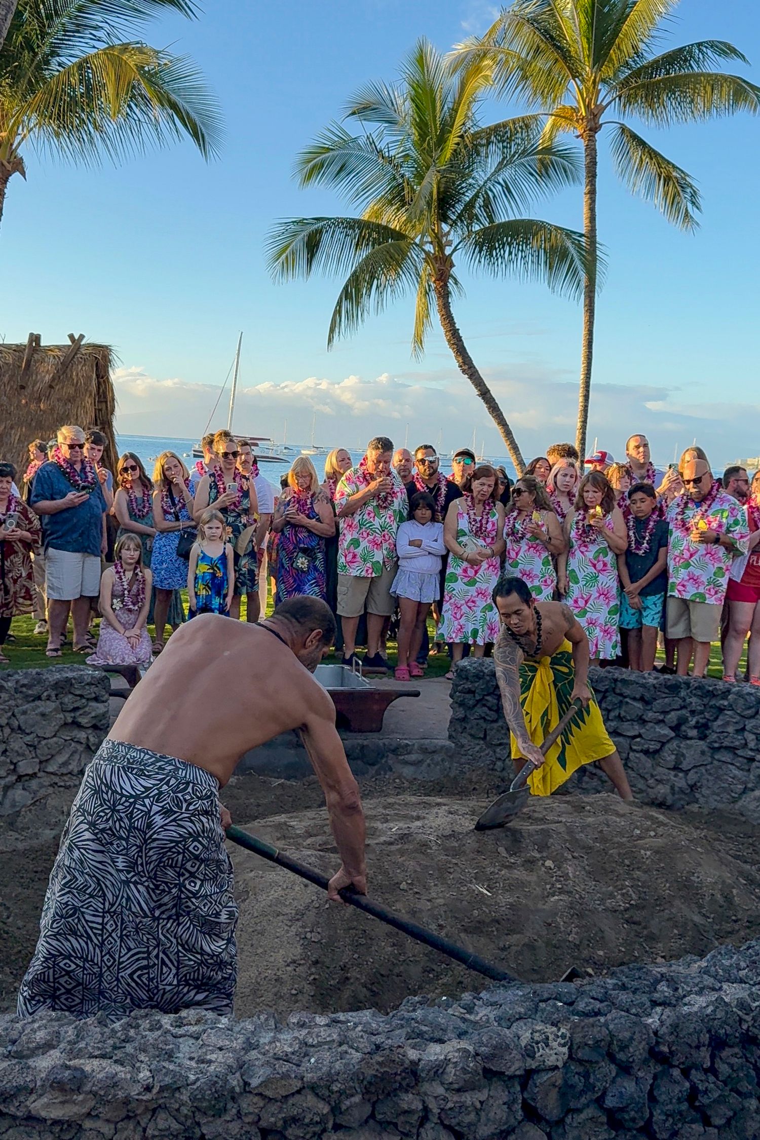 Beachside luau gathering at sunset with palm trees and volcanic rocks framing the festive scene.