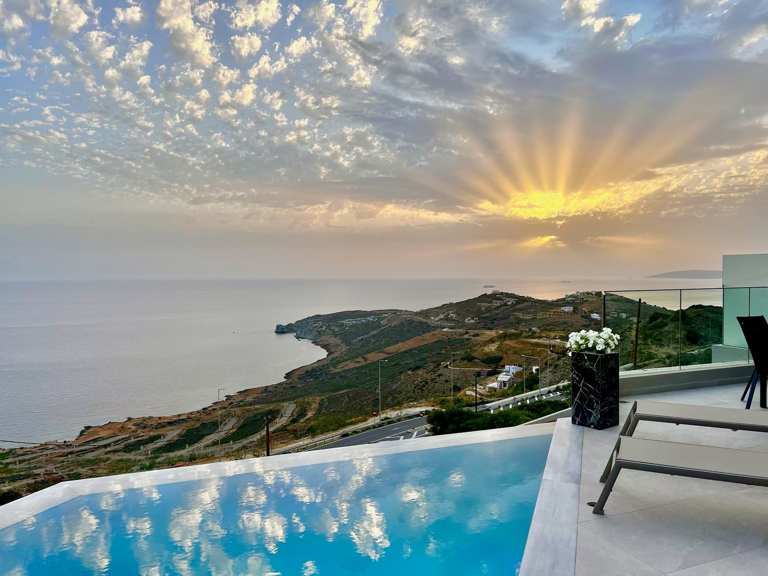 Infinity pool overlooking coastal mountains during golden hour with dramatic cloud formations.