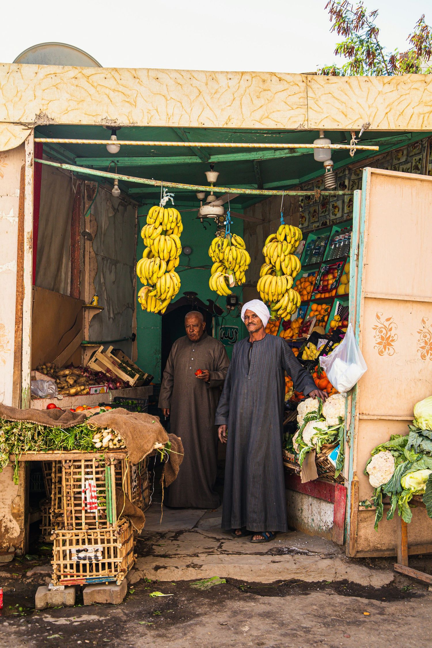 Traditional Egyptian market stall with hanging banana bunches and produce on display.