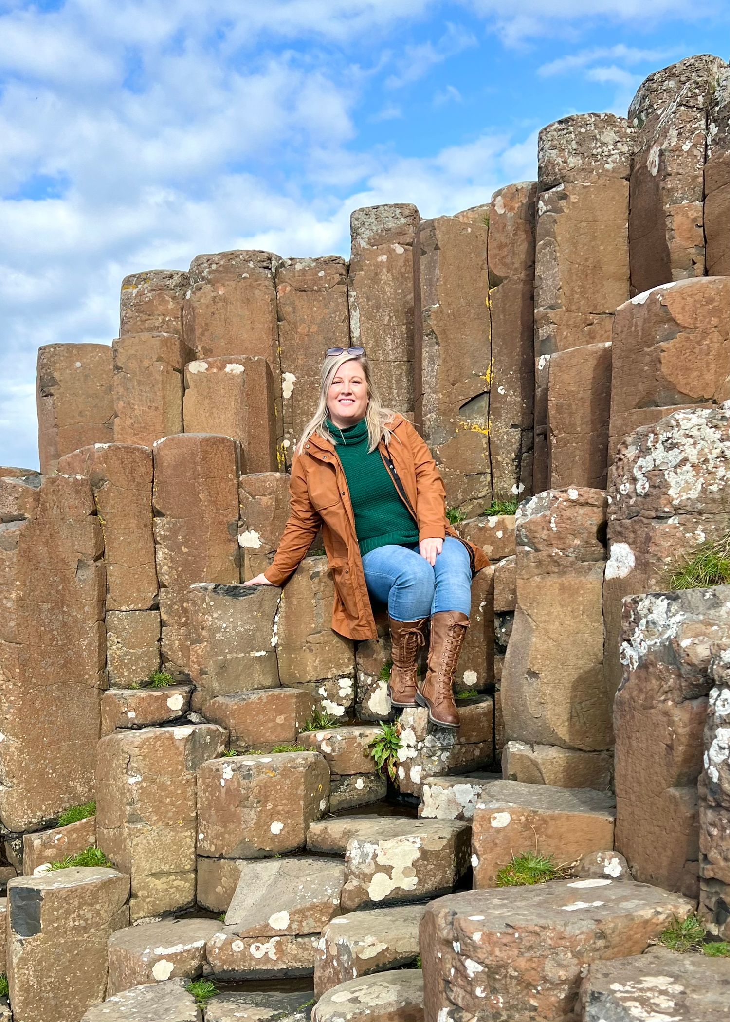 Person climbing on ancient basalt columns at Giant's Causeway in Northern Ireland under cloudy skies.