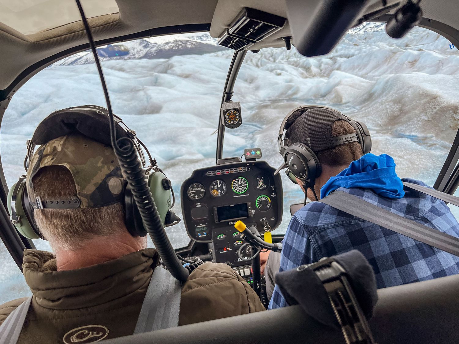 Cockpit view of a small aircraft flying over snowy glacier terrain.