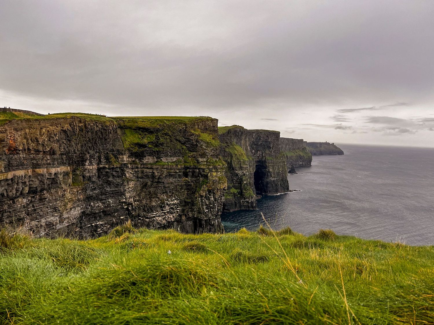 Dramatic coastal cliffs stretch along the misty Irish coastline under cloudy skies.