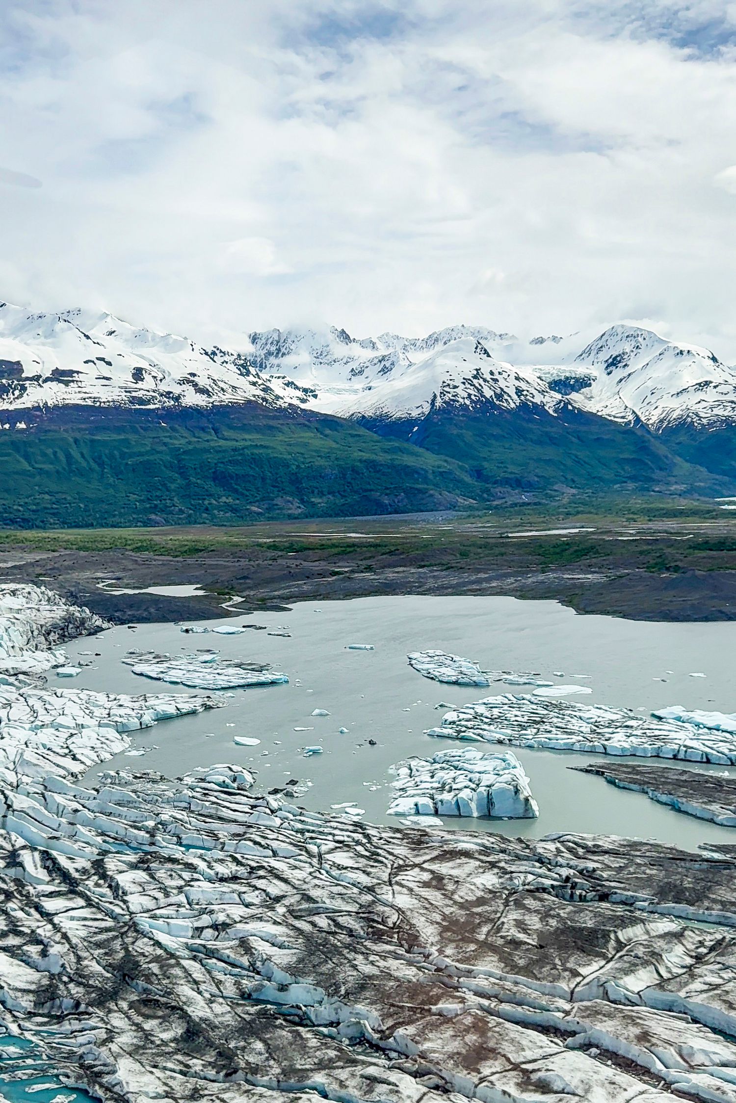 Panoramic view of a glacier-fed lake with floating icebergs and snow-capped mountains in the background, Knick Glacier.