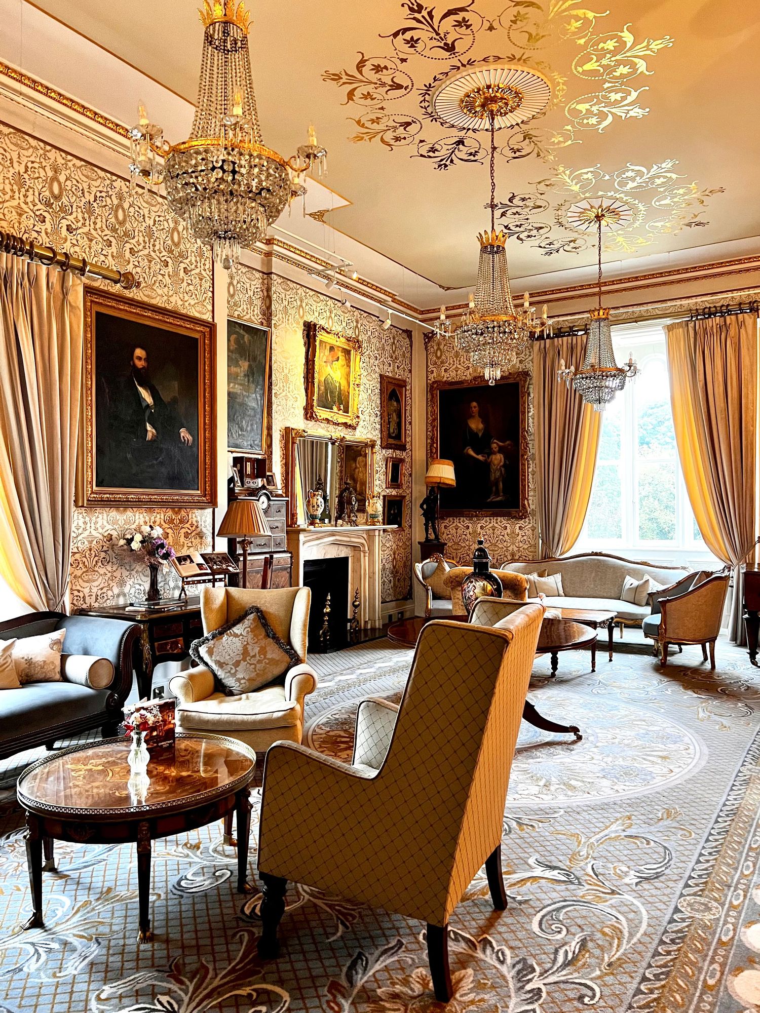 Elegant Victorian-style parlor room with ornate ceiling details, crystal chandeliers, gold-framed mirrors and plush upholstered furniture.