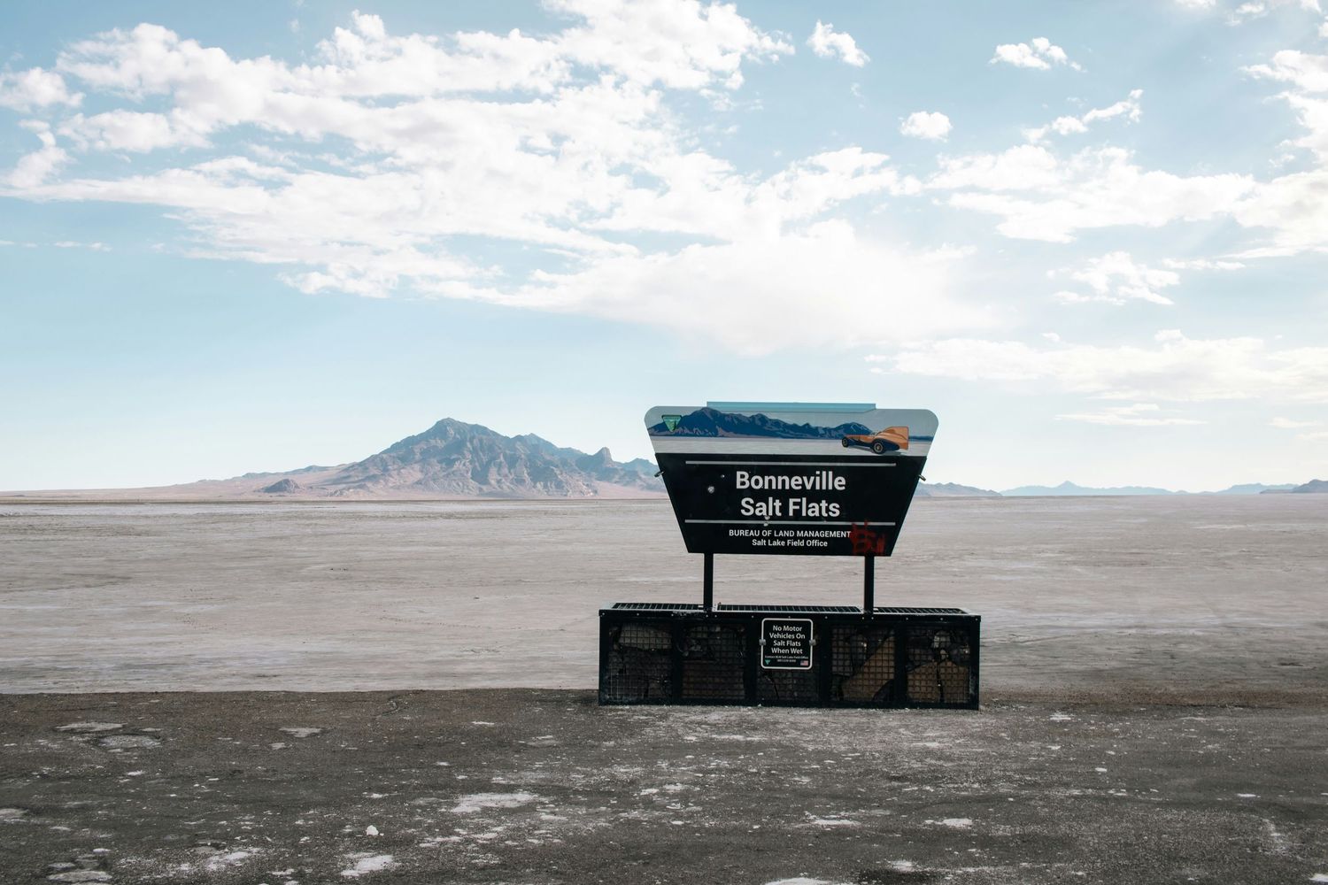 Desert landscape with information signs under bright blue sky and white clouds.