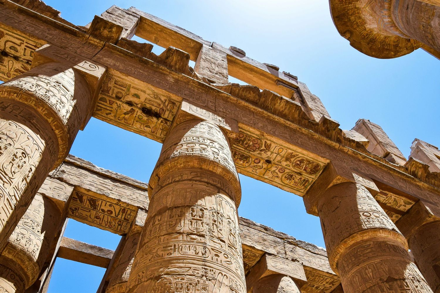 Massive stone columns with intricate carvings at an ancient Egyptian temple under bright sunlight.