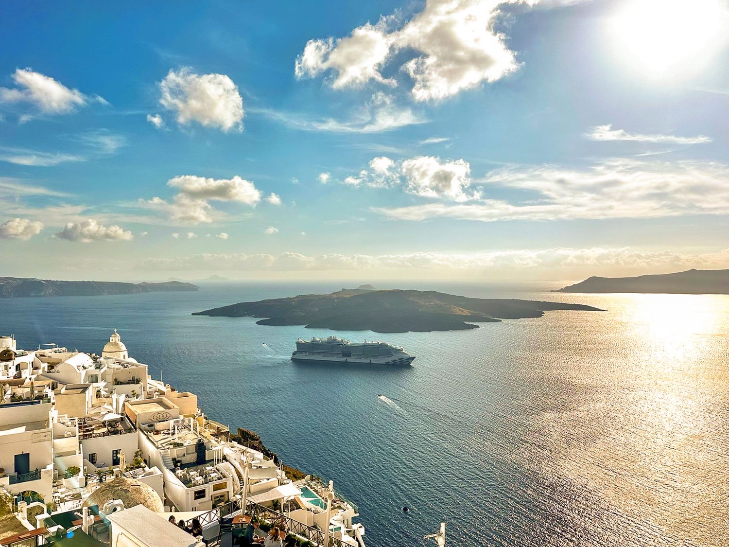 White cliffside buildings of Santorini overlook the Aegean Sea with cruise ships in the distance.