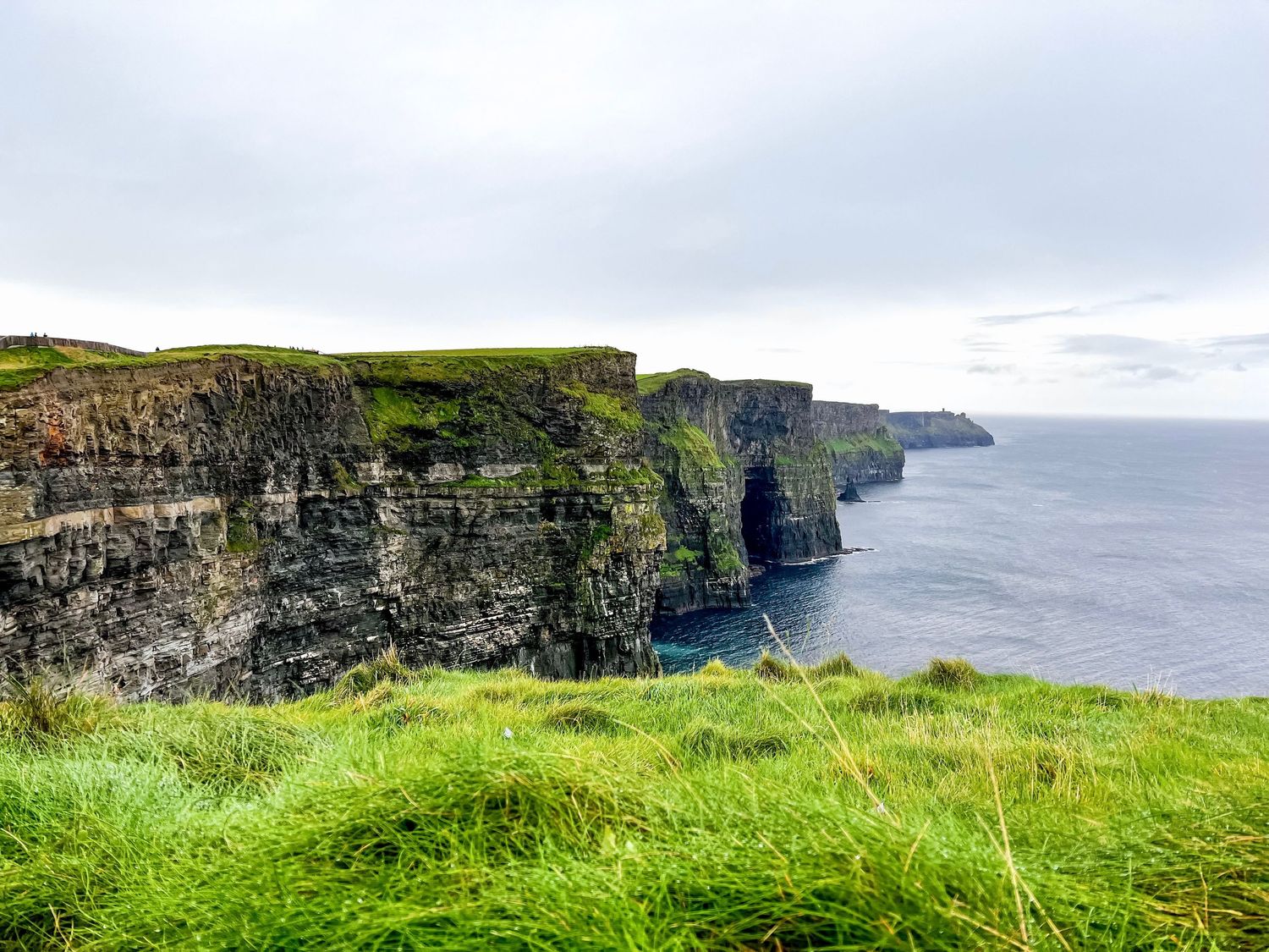 Panoramic view of the dramatic Cliffs of Moher in Ireland stretching along the Atlantic coastline under cloudy skies.