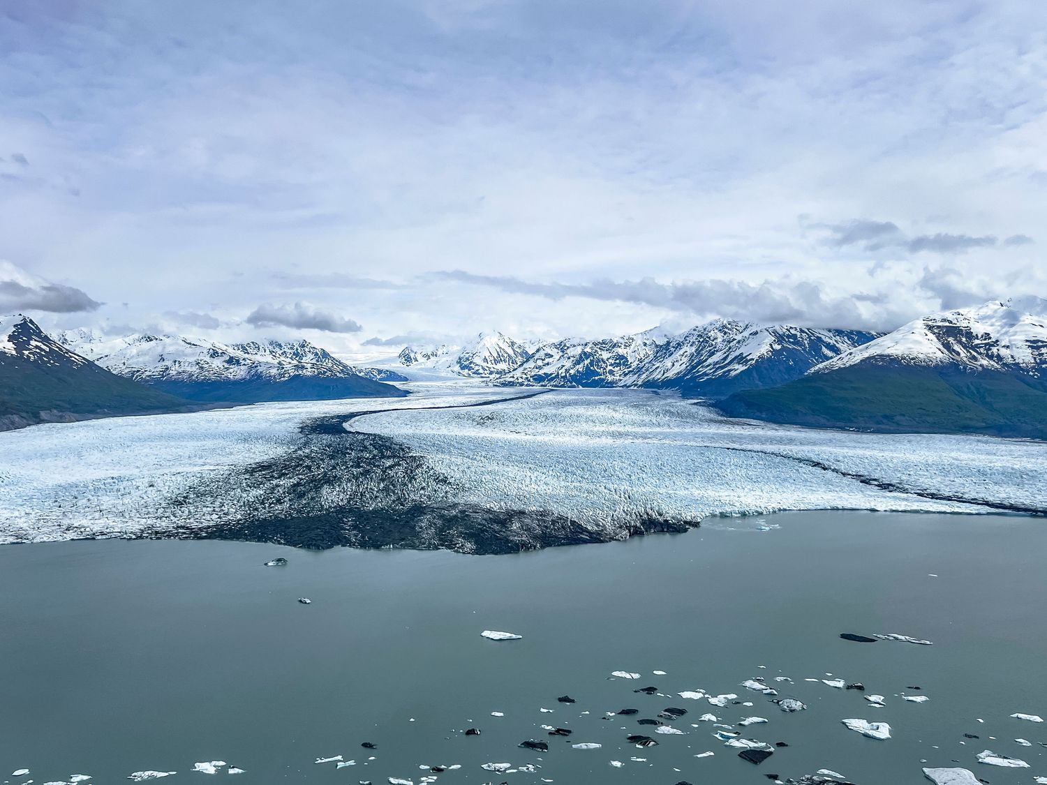 Snow-capped mountains rise above a glacial fjord with floating ice chunks scattered across the calm waters.