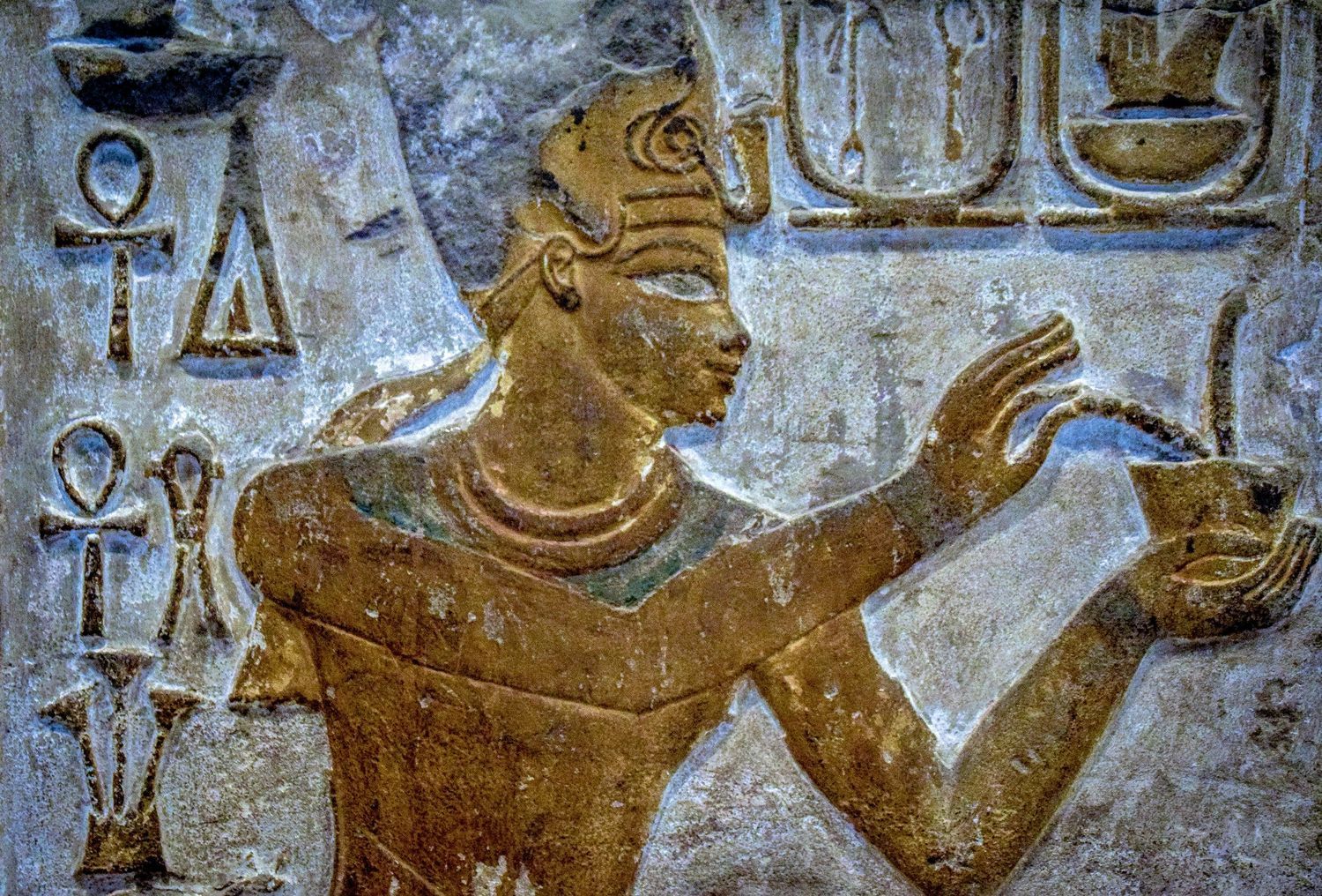 Ancient Egyptian wall relief showing hieroglyphic carvings and figures in traditional style with gold and blue coloring.