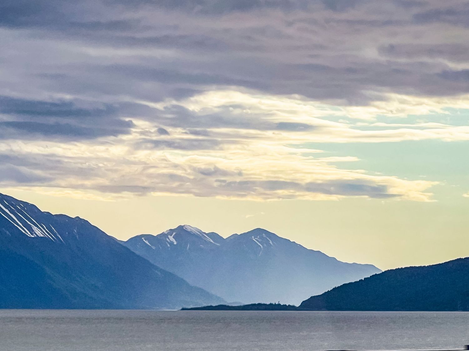 Dramatic sunset over snow-capped mountain ranges reflecting on calm waters in Alaska.