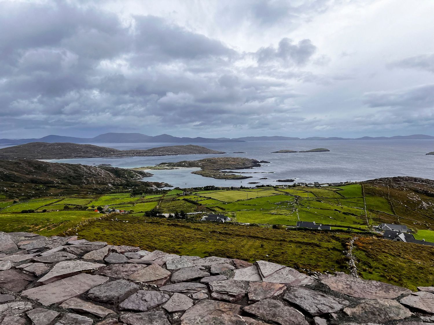 Rocky coastal landscape in Ireland with green fields and islands visible in the distance.