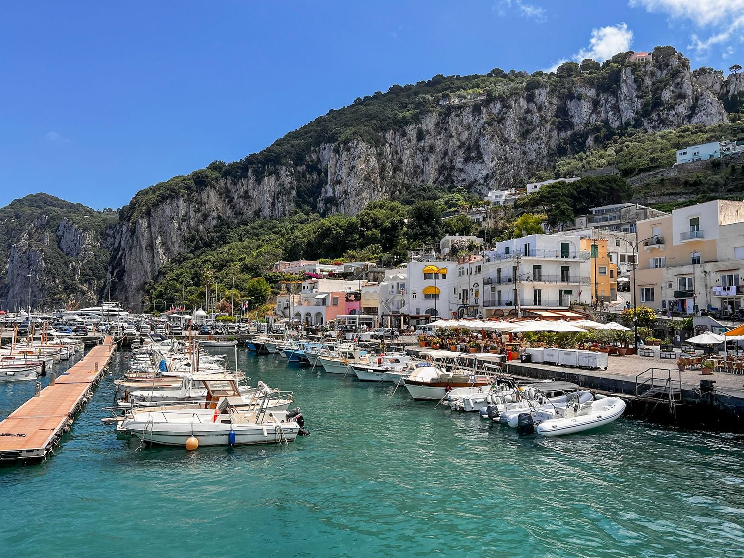 Colorful Mediterranean harbor with boats moored along steep cliffs and waterfront buildings.