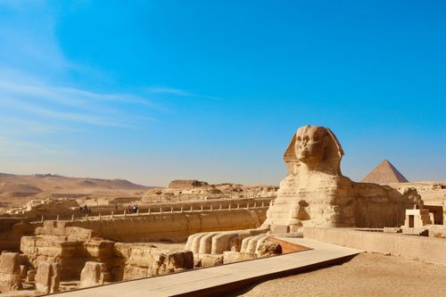 Ancient Egyptian Sphinx and pyramids at Giza stand majestically against a bright blue desert sky.