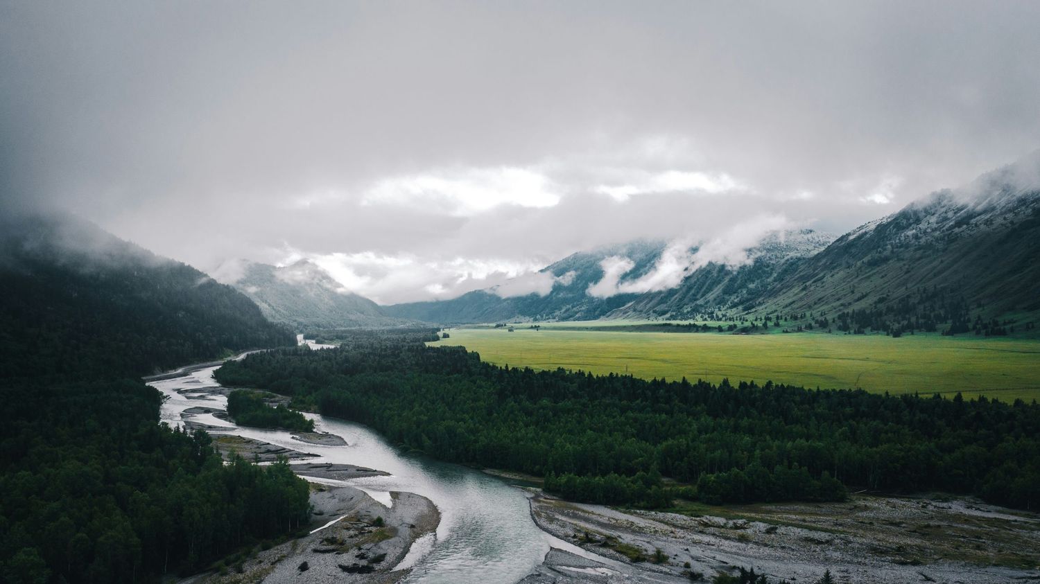 Expansive aerial panorama of a winding river valley through mountainous Alaskan terrain.