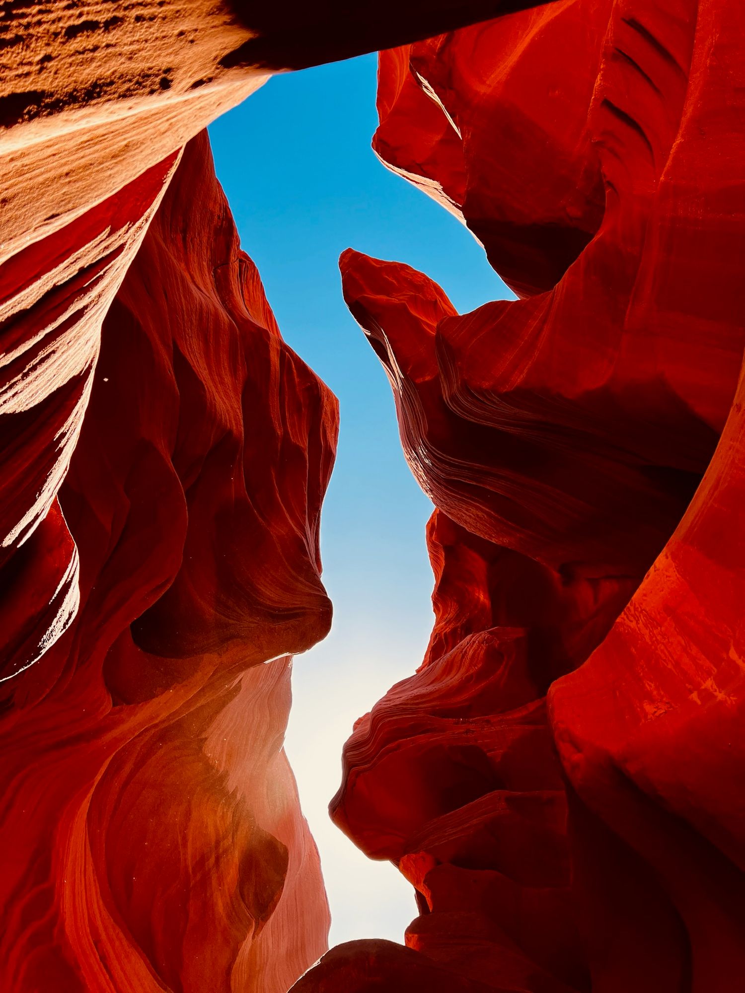 Stunning orange sandstone rock formations in Lower Antelope Canyon with bright blue sky peeking through narrow openings.