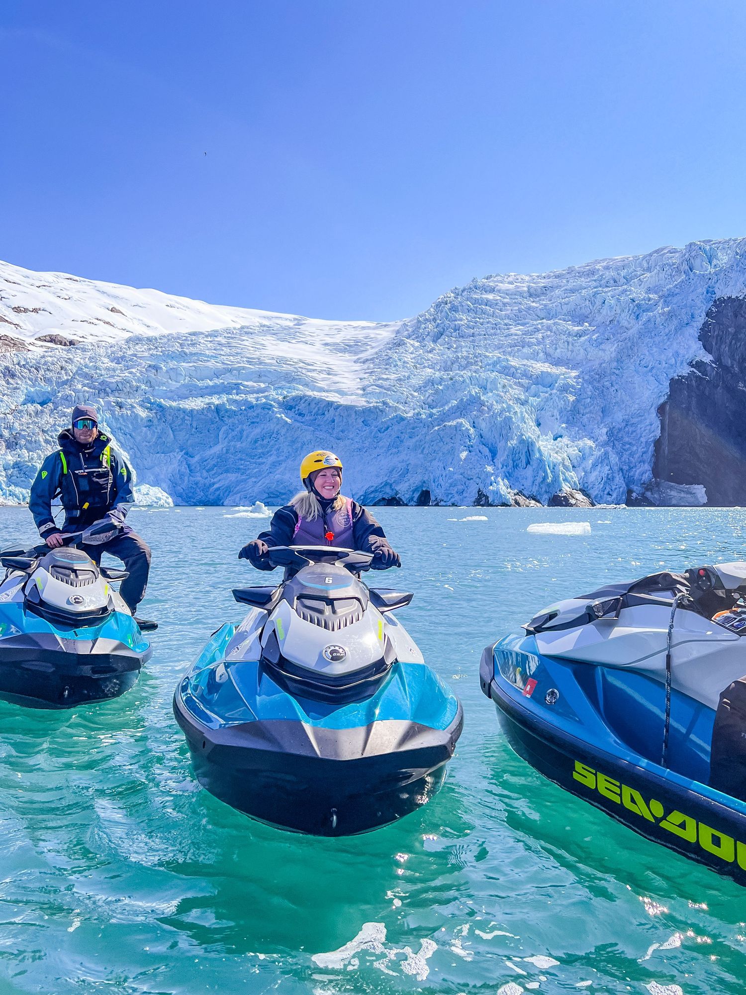Jet skis float on turquoise glacier waters surrounded by massive ice walls.