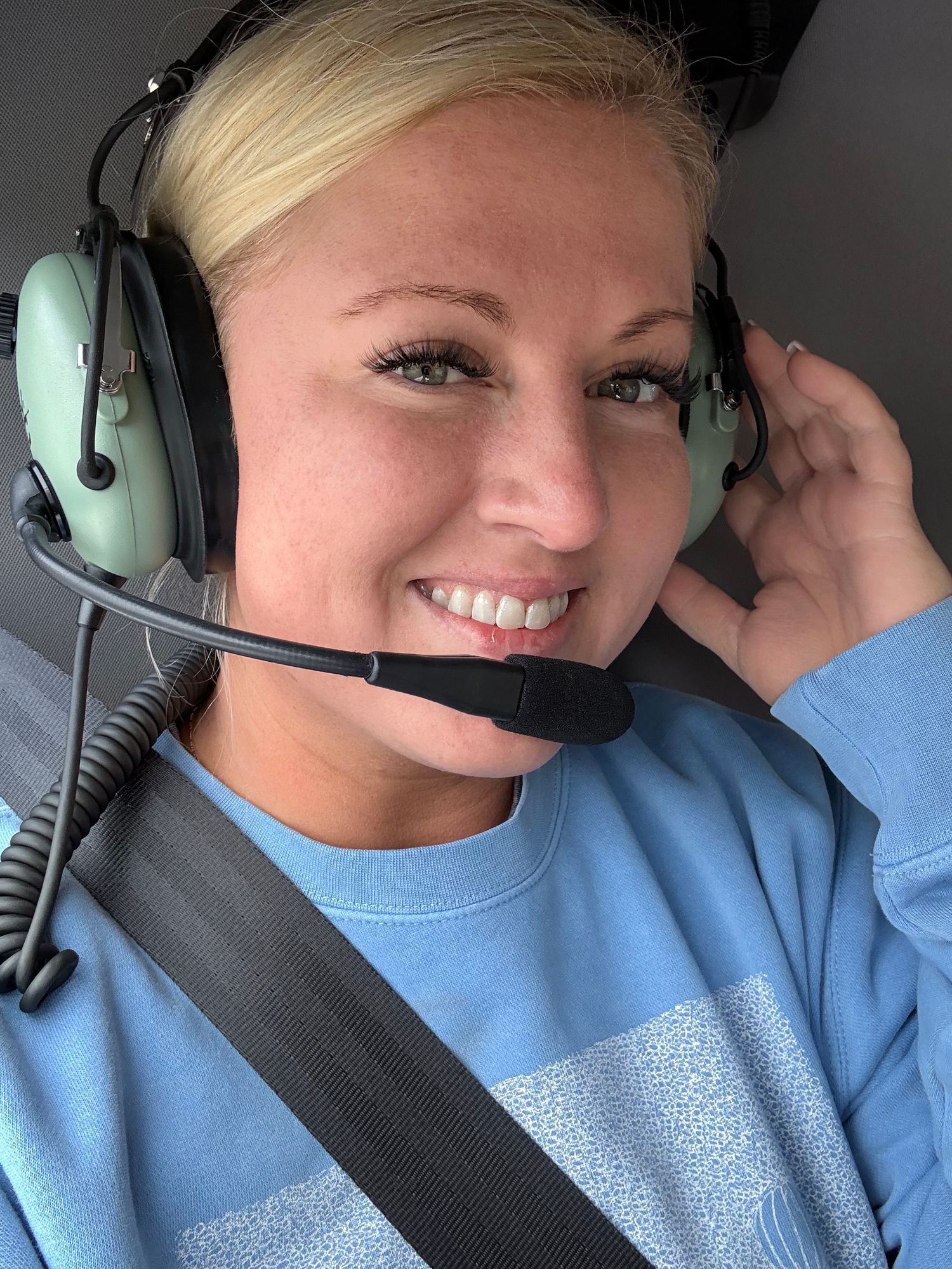 Selfie view of someone wearing aviation headphones while sitting in an aircraft cockpit.