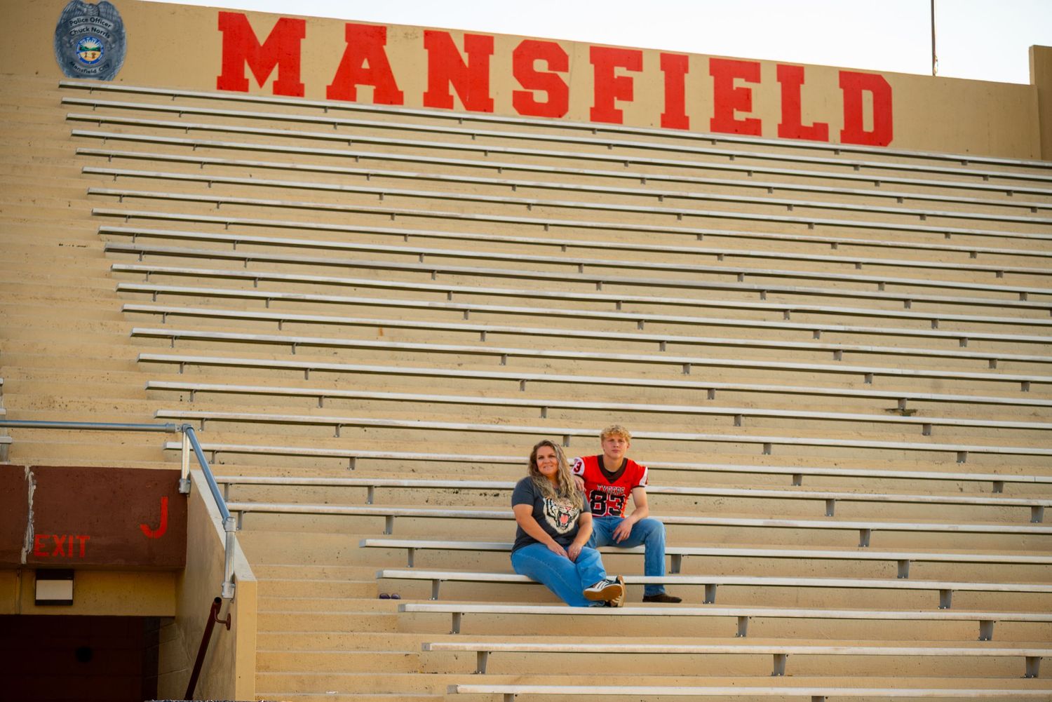 Two people sitting in the bleachers at Mansfield stadium on a sunny day.
