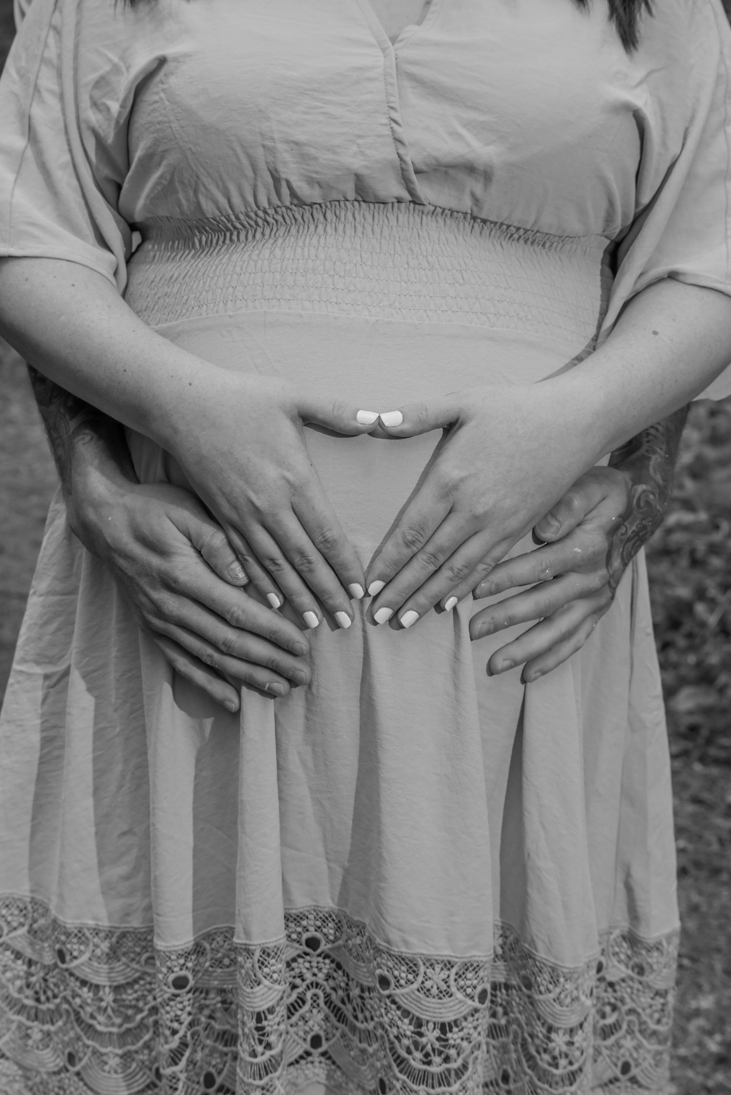 Black and white photo of pregnant woman with two sets of hands forming heart shape on baby bump.