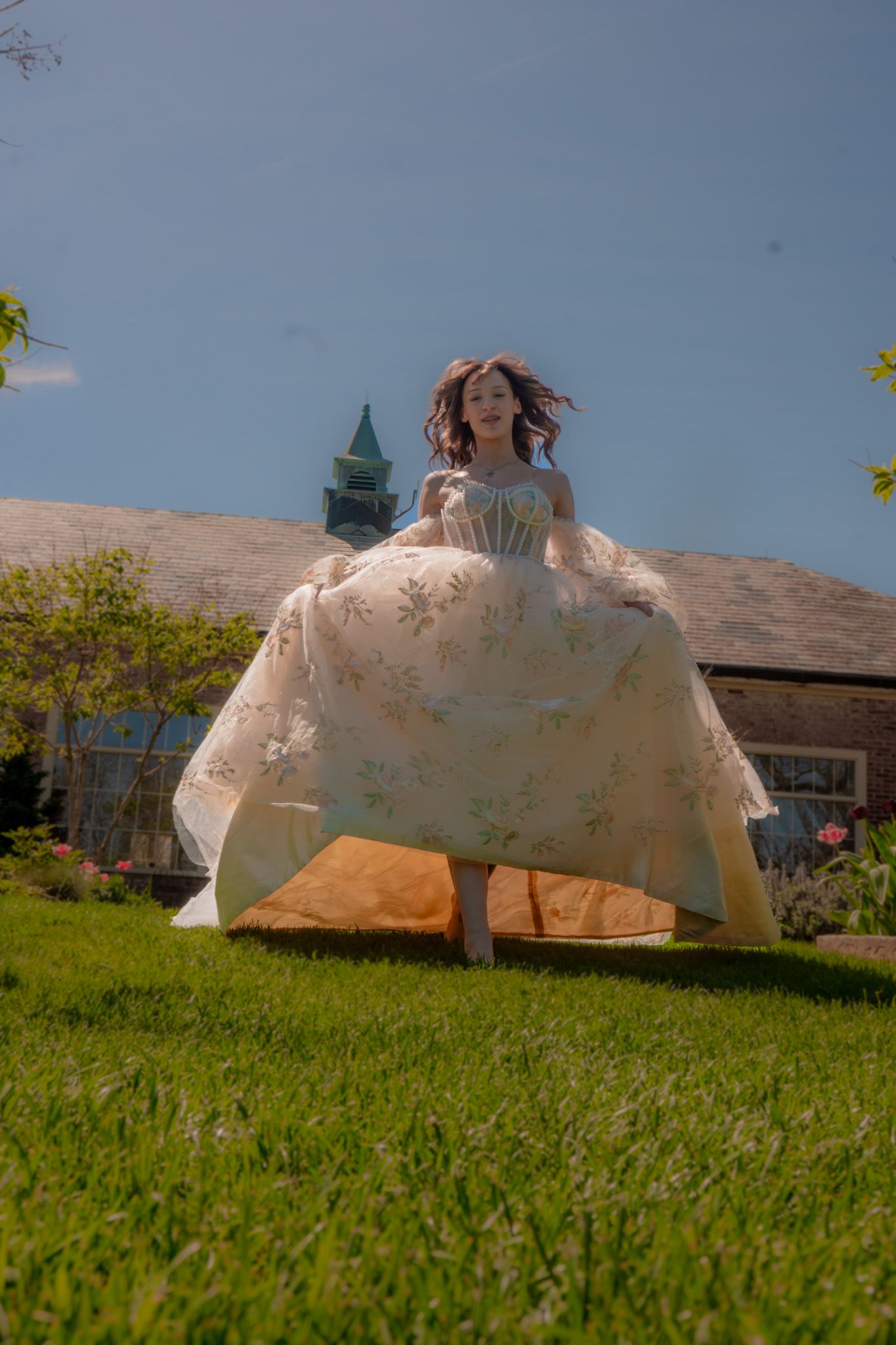 Two figures in white dresses lay on a grassy hillside under a blue sky, creating a dreamy outdoor scene.