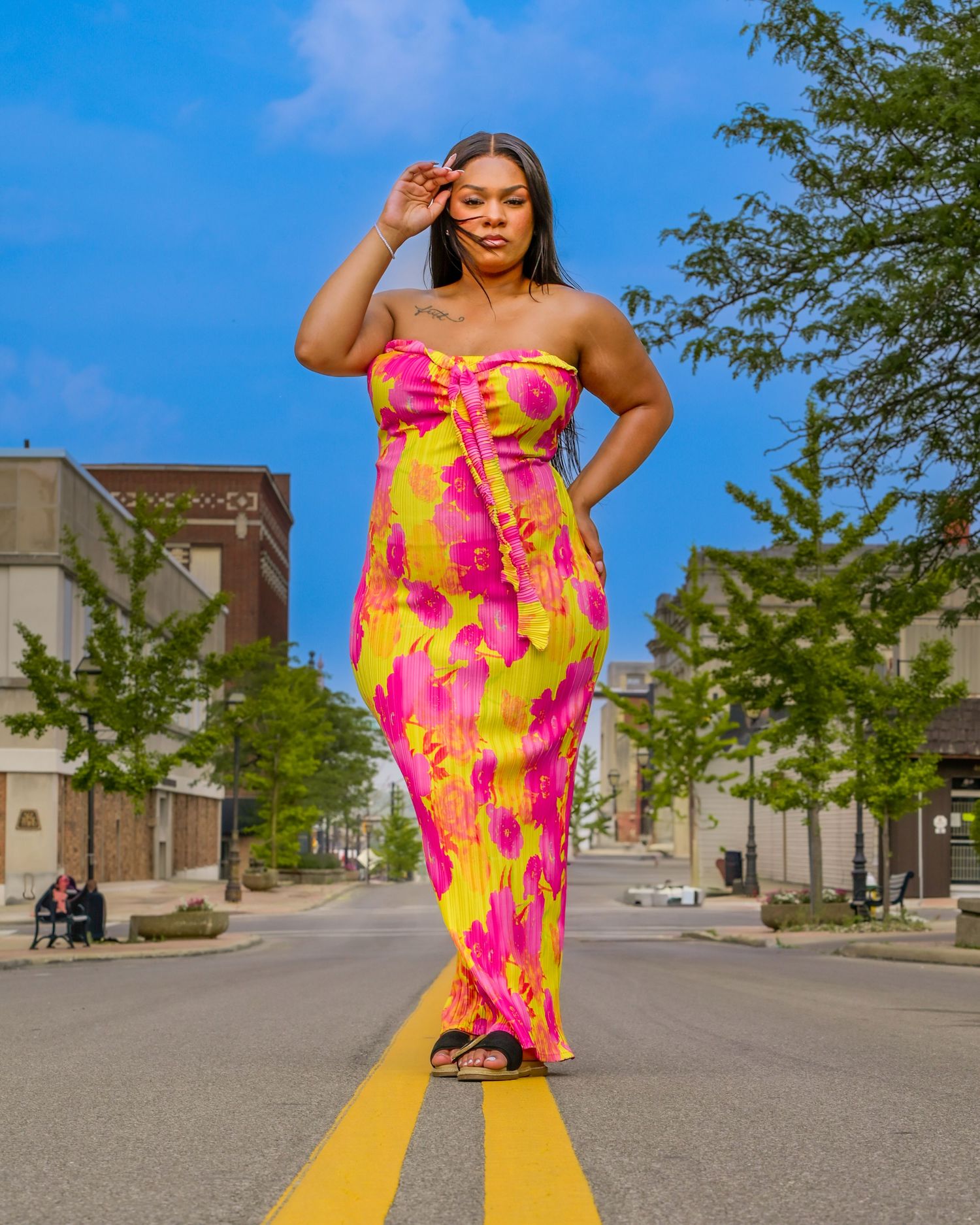 A person in a vibrant yellow and pink tie-dye maxi dress poses confidently on a sunny street.