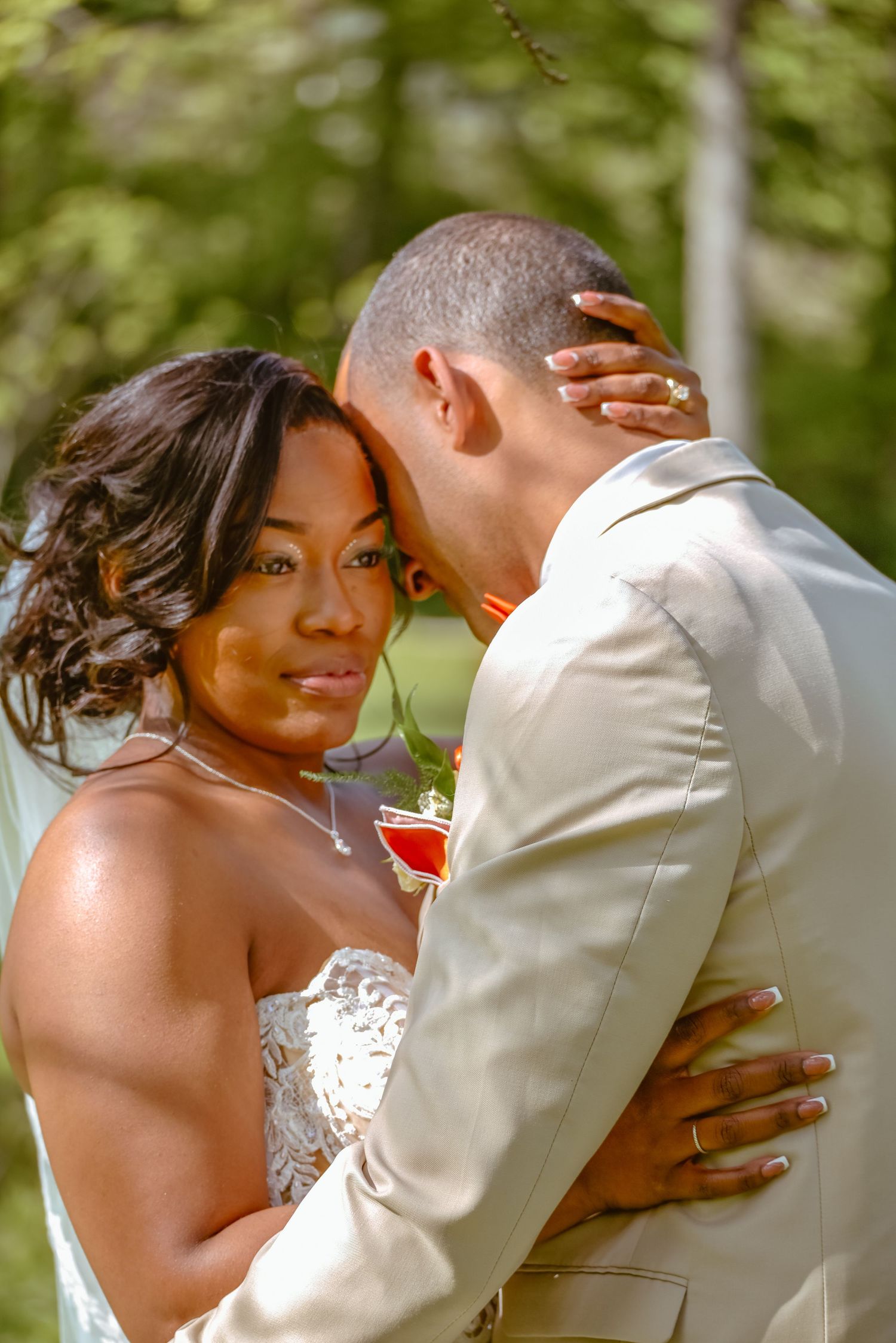 Bride and groom share a romantic embrace outdoors, with the bride in a white strapless gown smiling at the camera.