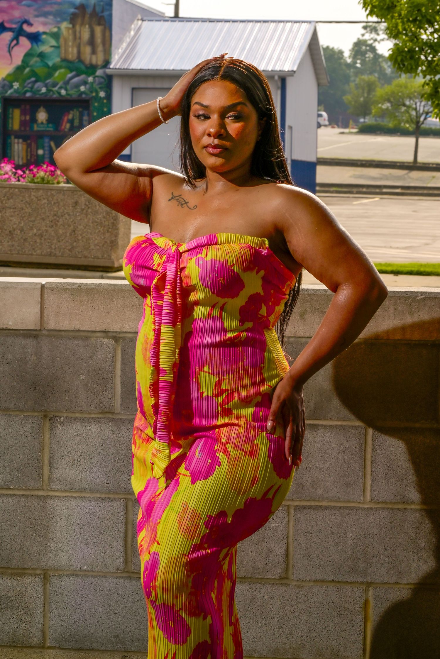 Vibrant pink and yellow floral print strapless dress worn in an outdoor urban setting during golden hour.