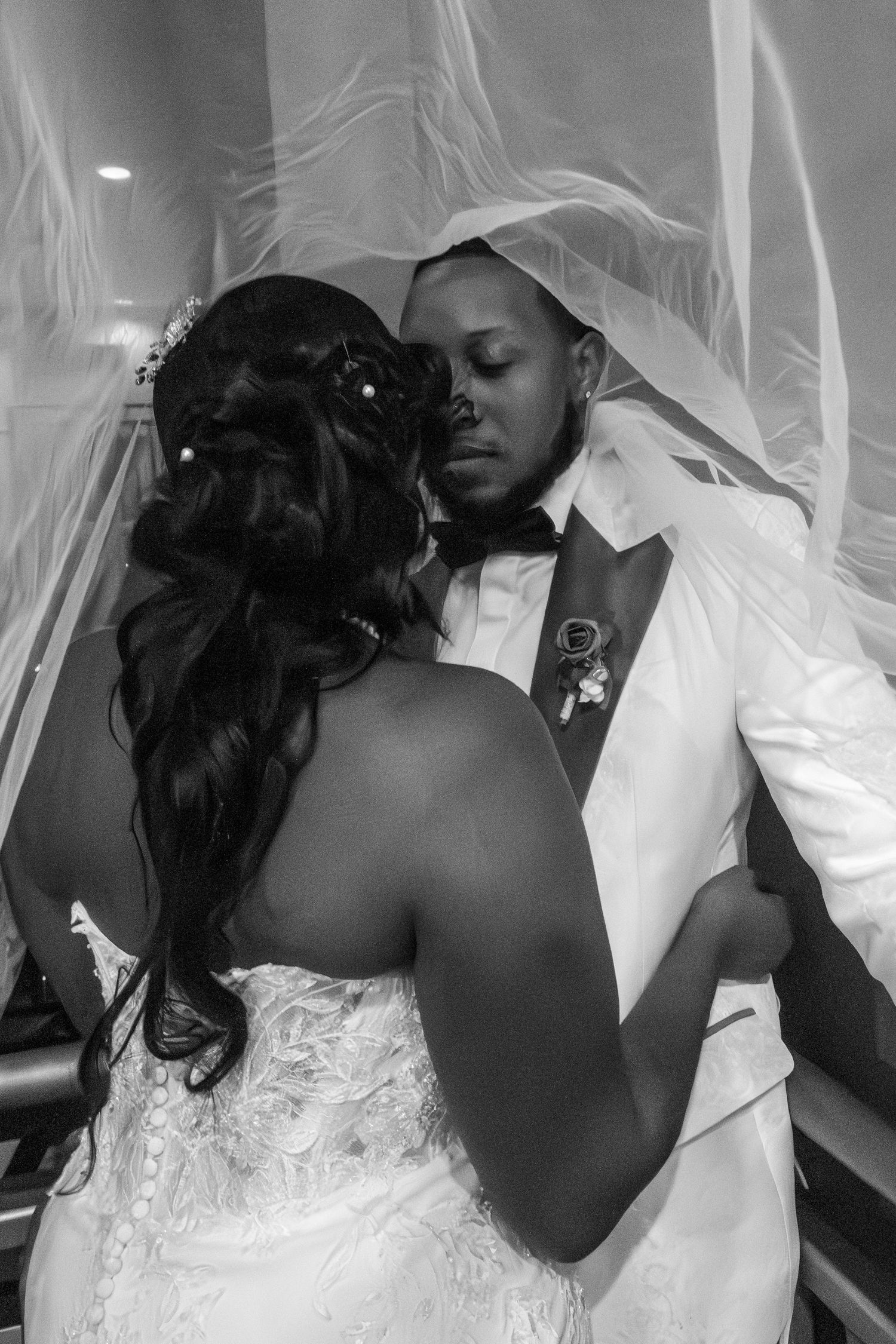 Black and white wedding photo of bride and groom sharing intimate moment under veil on staircase.