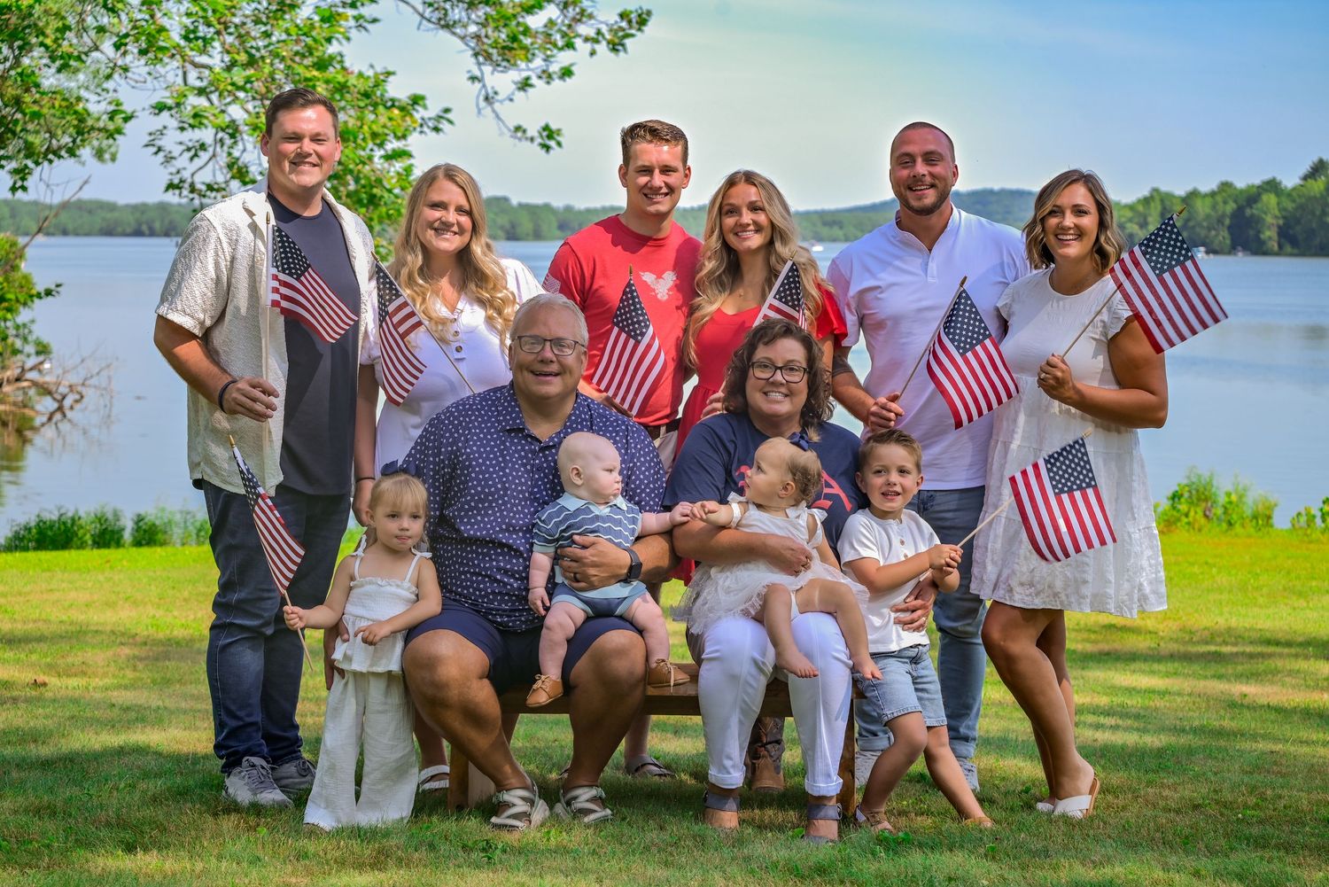 Family group photo with American flags by a lake on a sunny day.
