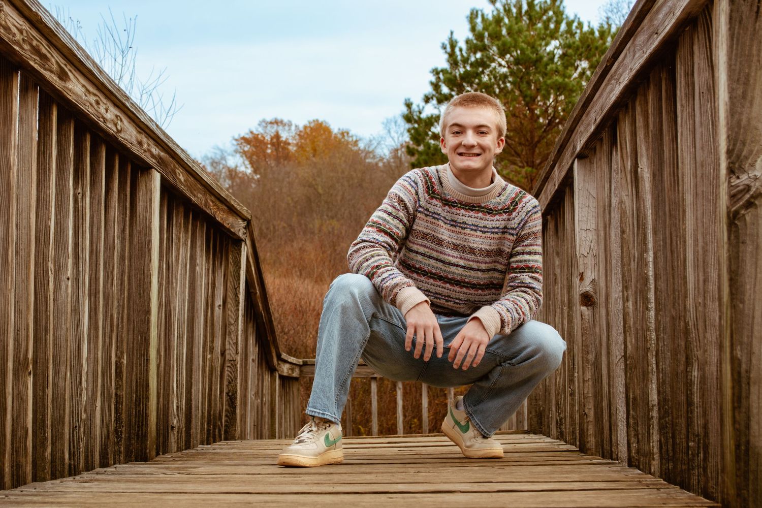 Casual autumn portrait on a wooden bridge with fall foliage in the background.