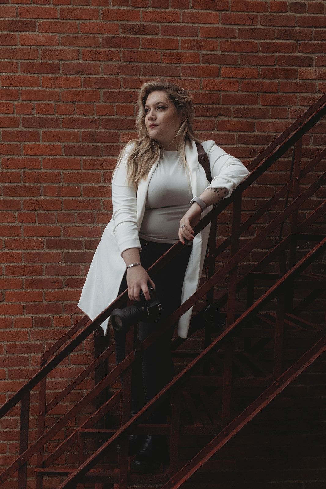 Fashion portrait of someone in a white coat posing on brick building stairs.