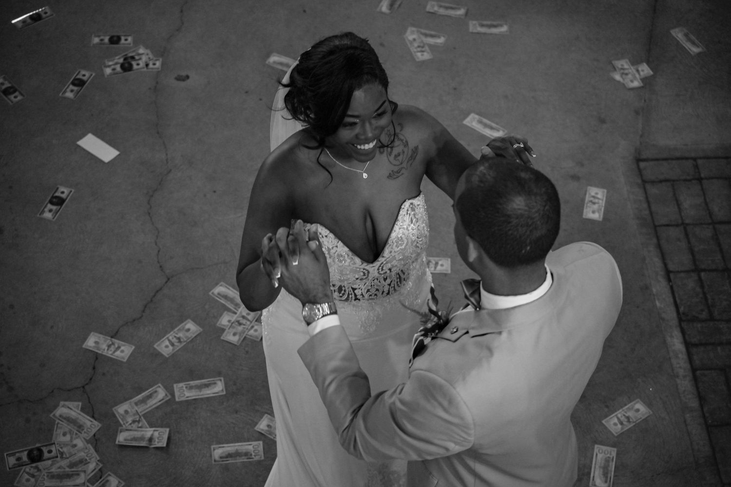 Aerial black and white photo of a bride and groom sharing a first dance surrounded by scattered dollar bills.