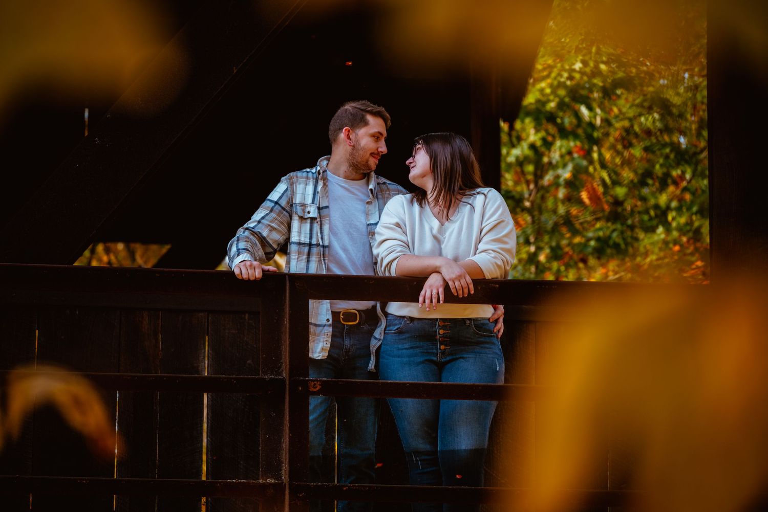 Romantic couple sharing a tender moment on a wooden balcony surrounded by lush greenery at night.
