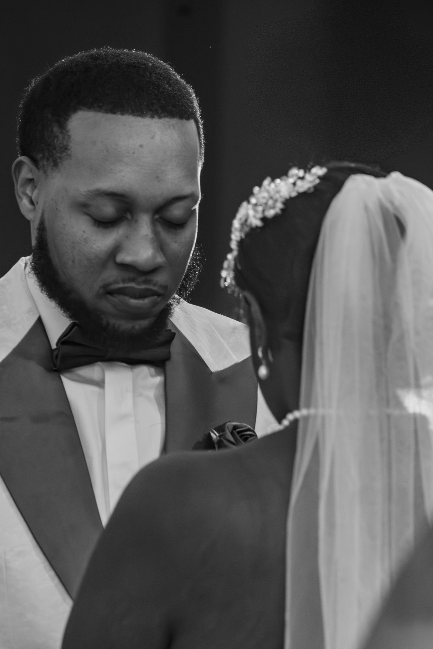 Black and white wedding photo of groom in bow tie looking down at bride in veil and crystal headpiece.