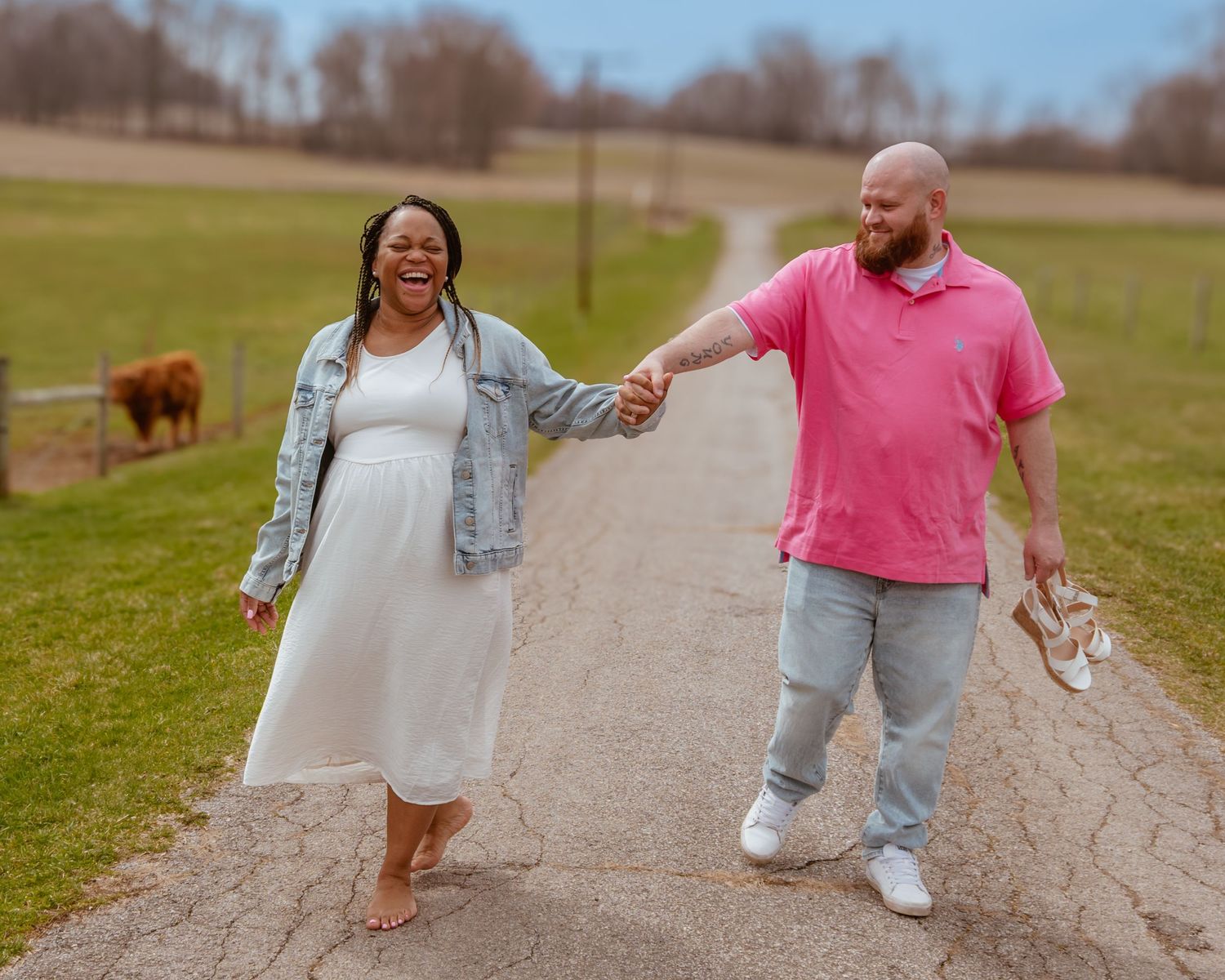 A couple walks hand in hand along a pathway with a Highland cow grazing in the background.