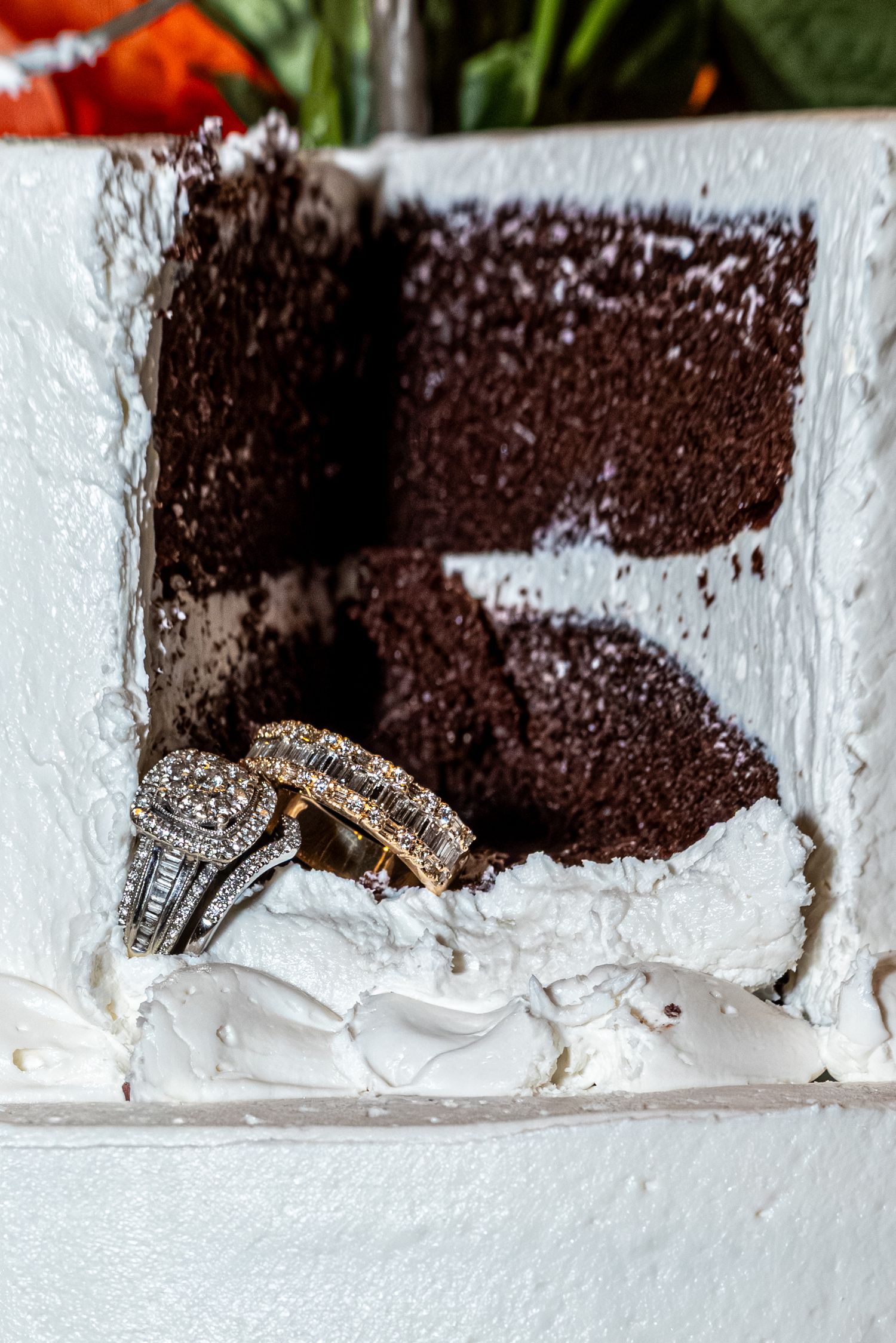Wedding rings resting in a slice of white frosted chocolate cake, perfect for wedding reception inspiration.
