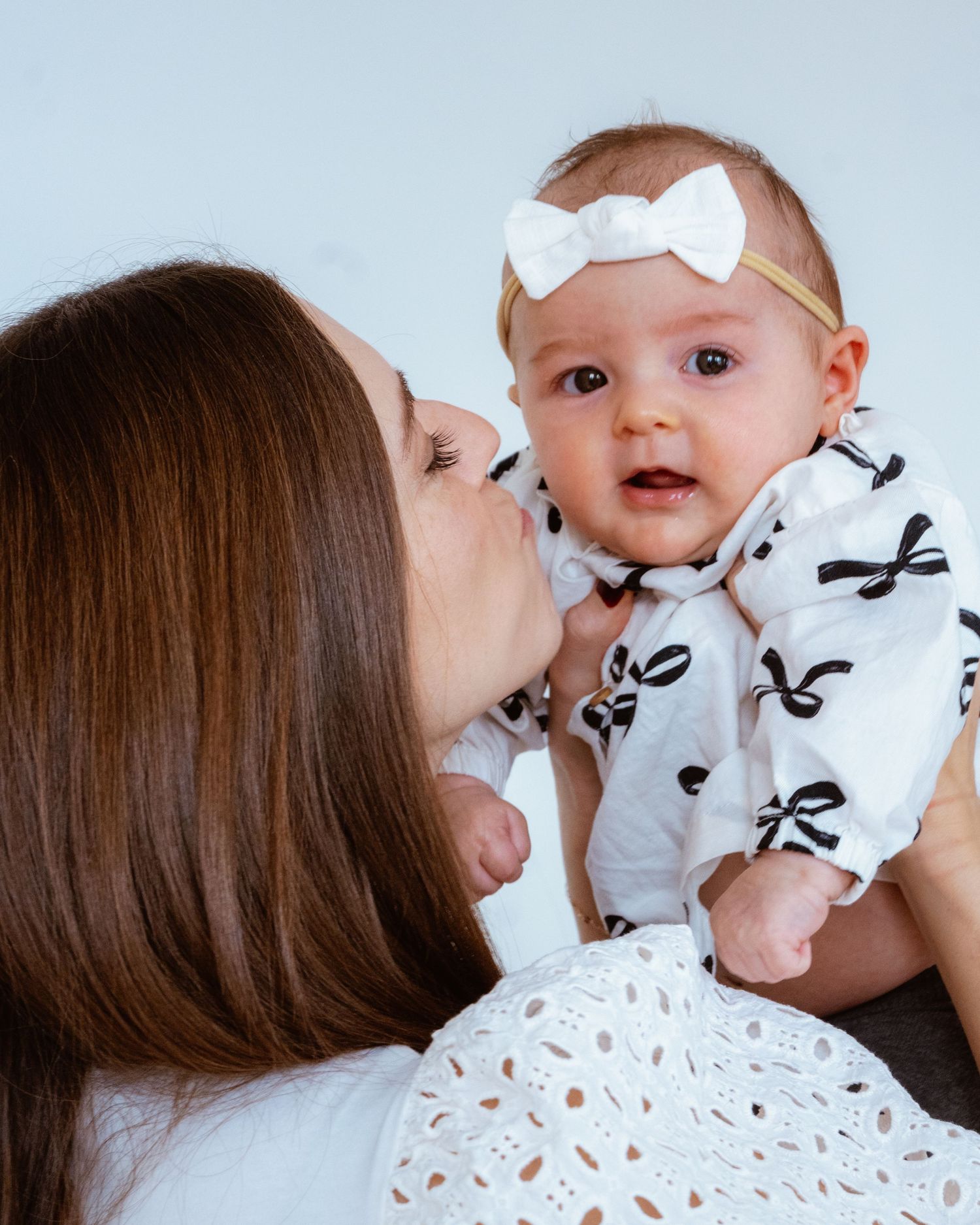 A tender moment between a mother and baby wearing a white bow headband and patterned onesie.