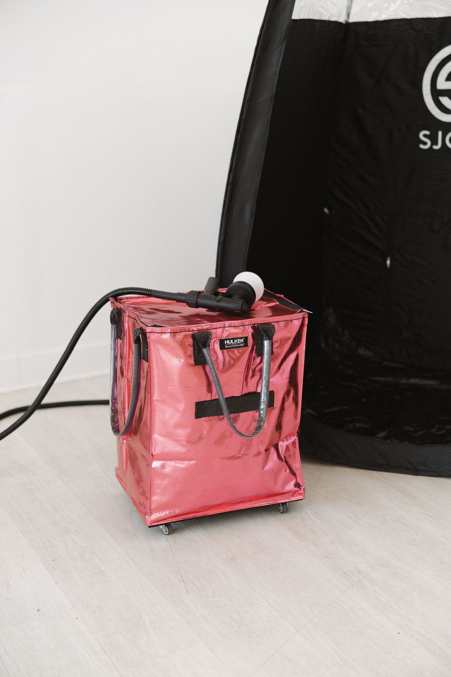 Pink translucent storage cube with black straps and spray attachment on light floor.