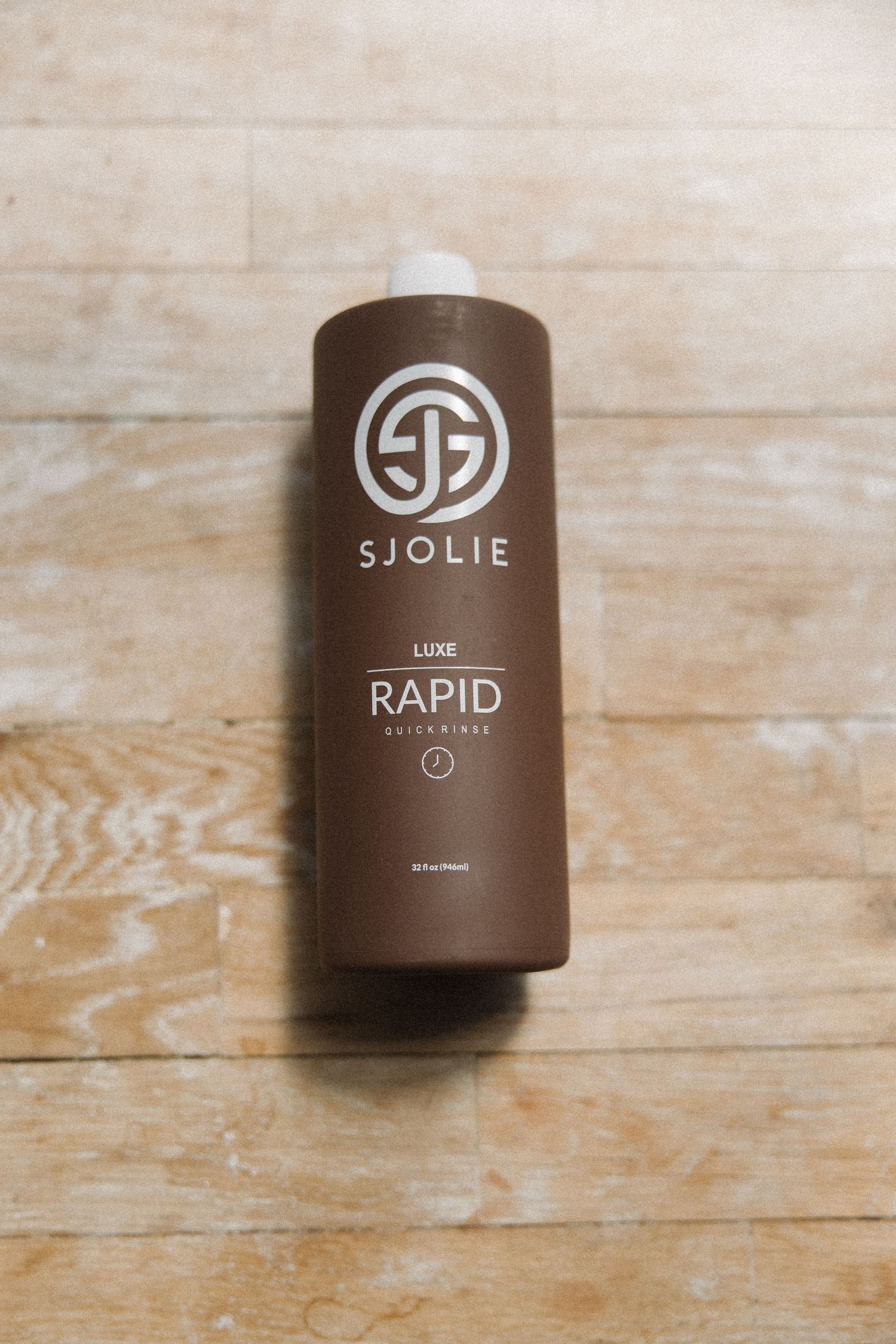 Brown bottle of Sjolie Rapid tanning solution with white logo displayed on wooden background.
