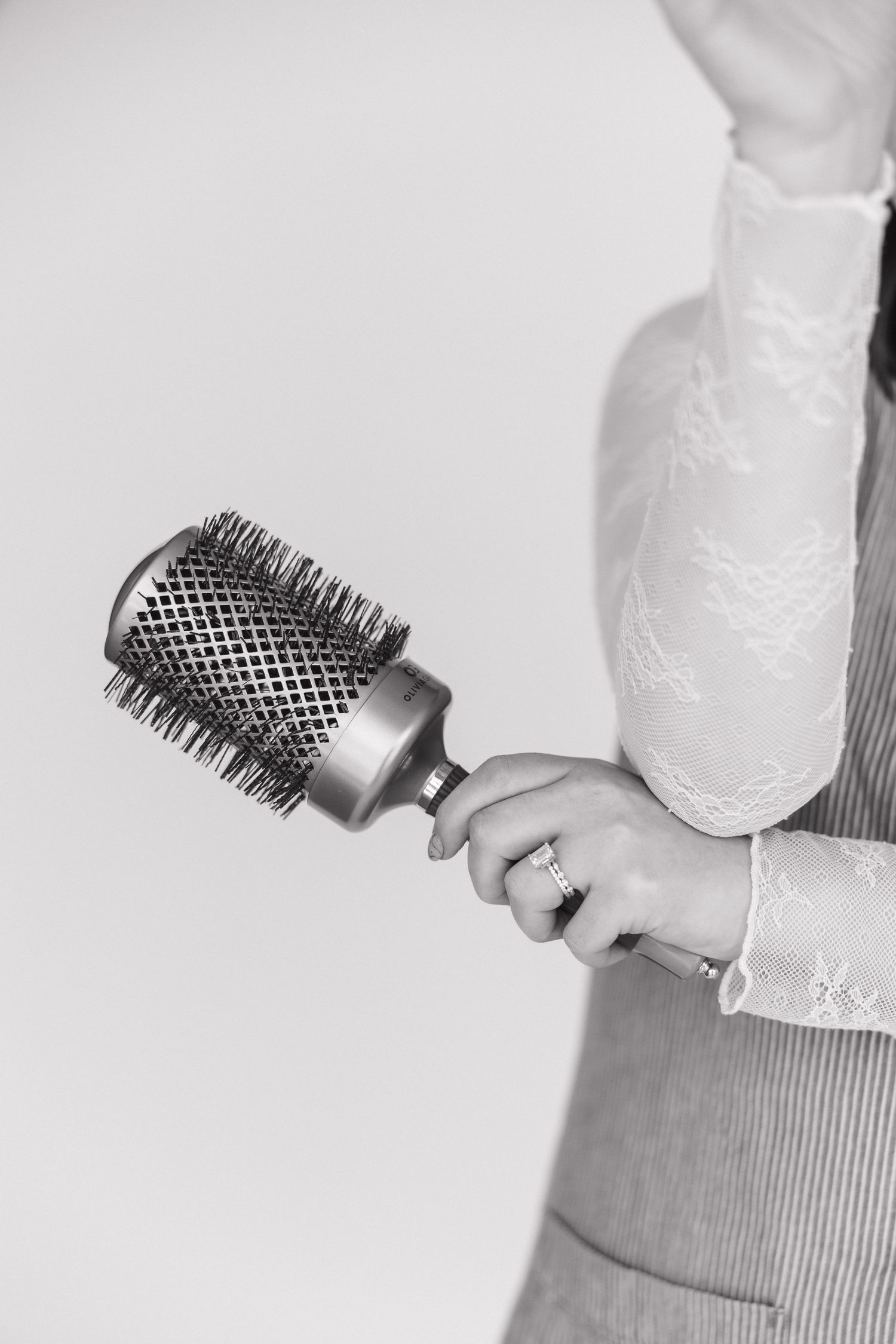 Close-up of hands holding round hair styling brush against white background.