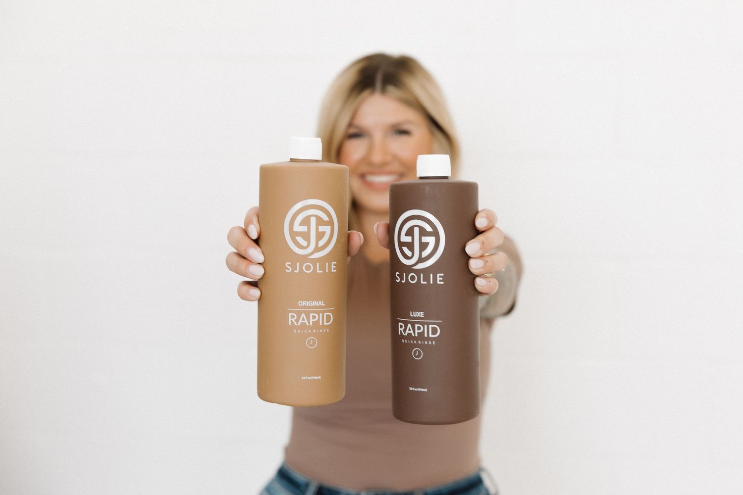 Two brown SJOLIE tanning product bottles being held up against a white background.