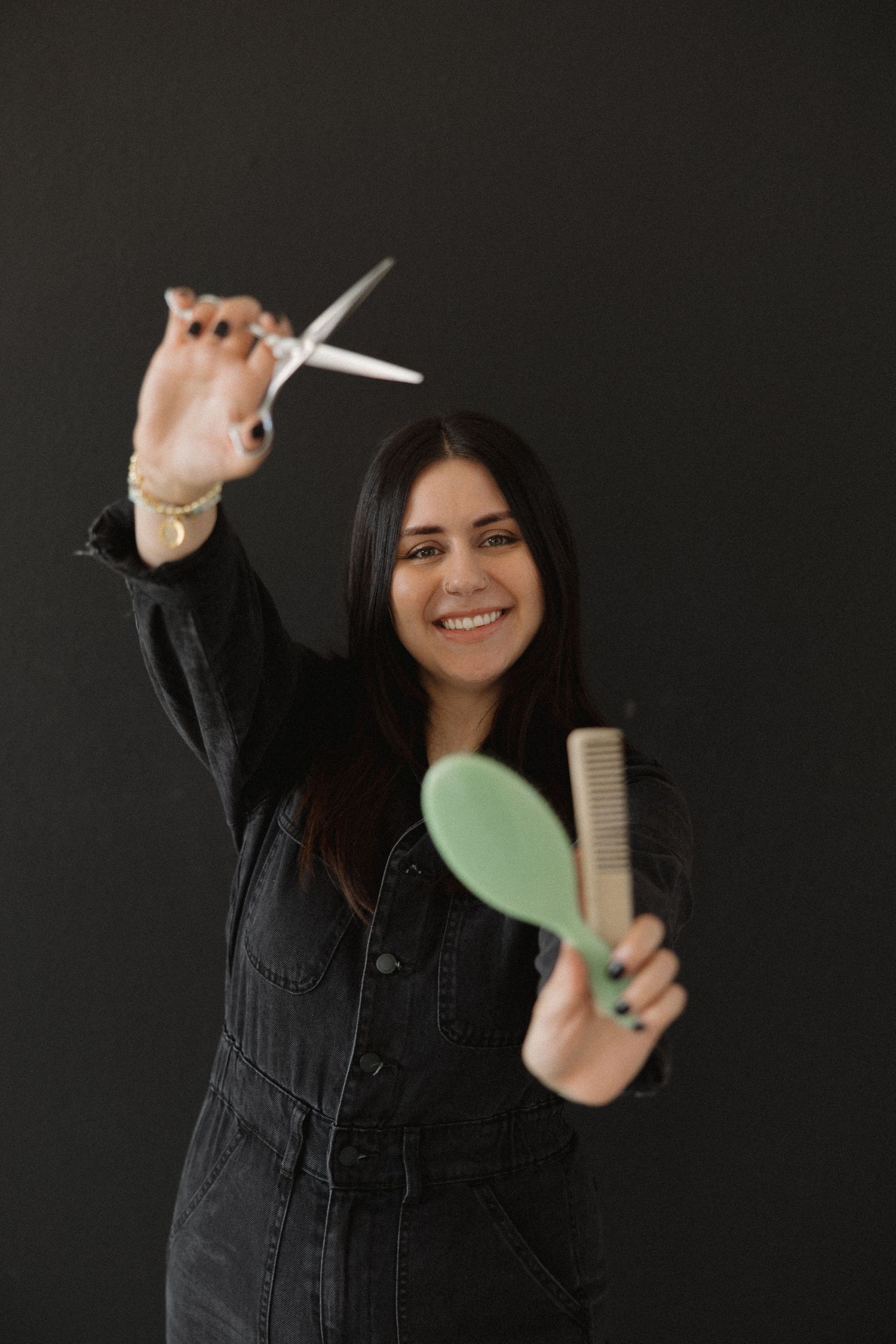 Hair professional demonstrates styling tools while wearing dark denim jumpsuit.